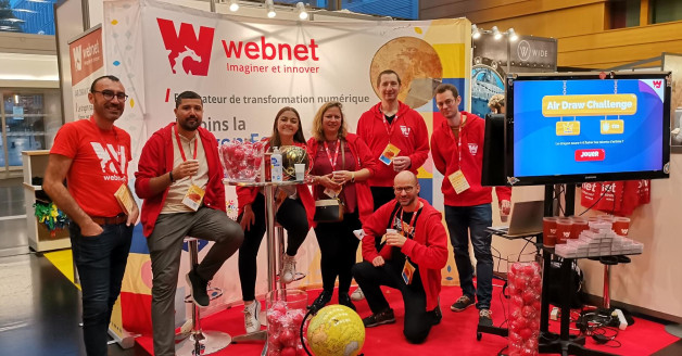 L'équipe de Webnet, prend la pose devant leur stand avec l'écran du jeu à côté